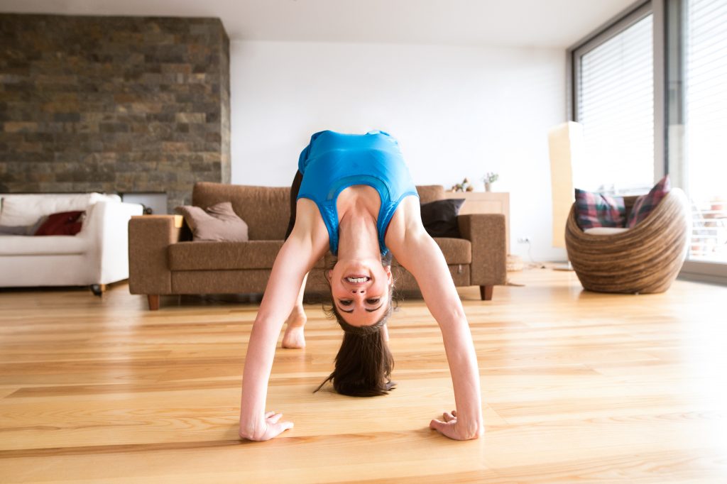 Beautiful young woman working out at home in living room, doing yoga or pilates exercise. Stretching, doing bridge pose.