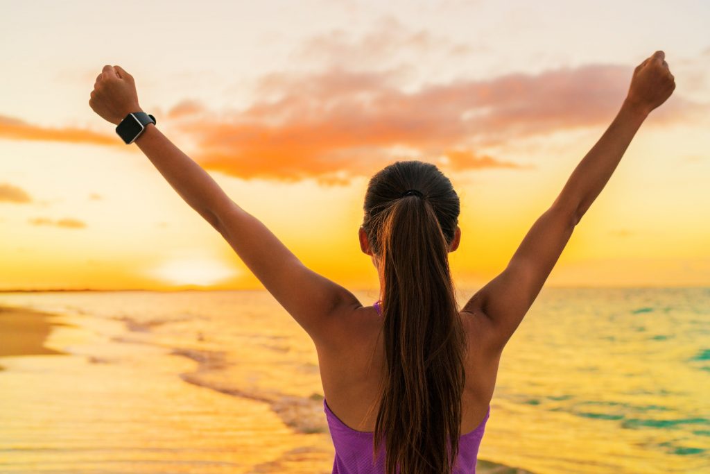 55651555 - success freedom smartwatch woman from behind at sunset. winning goal achievement fitness athlete girl cheering on tropical summer beach wearing wearable tech smart watch activity bracelet.